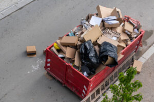 A waste container overflowed A steel industrial with rubbish on the street, Various types of waste, including empty carton boxes, plastic, and construction debris, New Office in urban waste management. construction site.